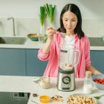 A woman in a kitchen preparing a nutritious smoothie with fresh ingredients.