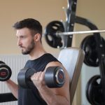 Focused man lifting dumbbells for bicep curls in gym, emphasizing strength and fitness.